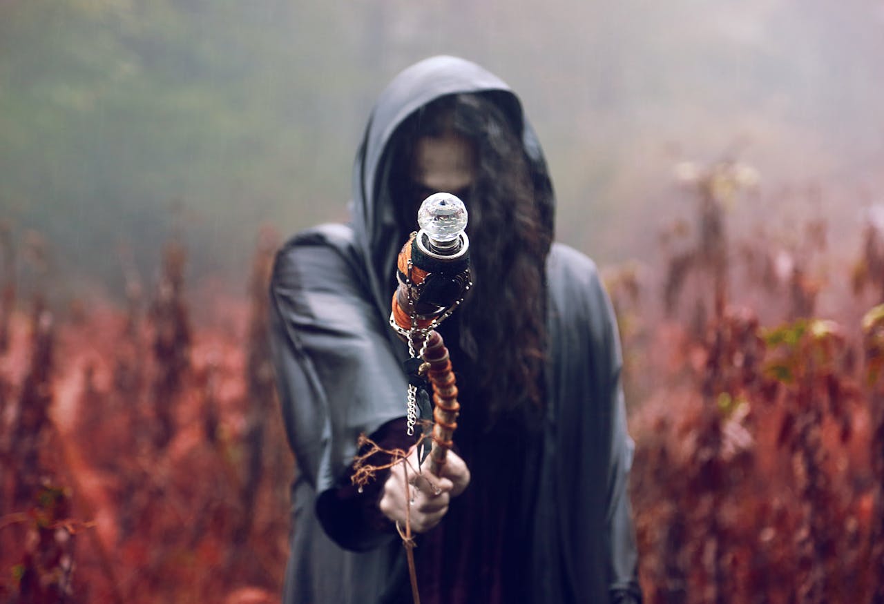 mobile-02 A hooded figure holds a staff in a misty, autumn forest setting, evoking mystery and fantasy.